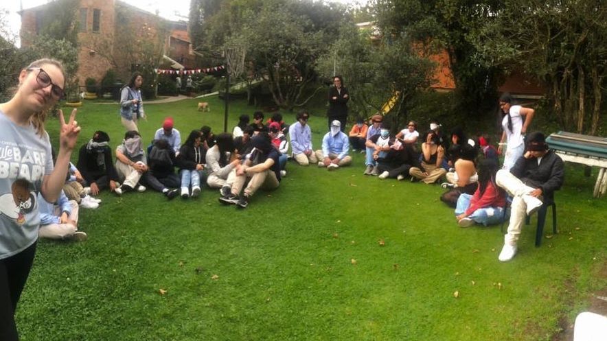Encuentro al aire libre: un grupo grande de jóvenes sentados en círculo sobre el césped de un parque, varios haciendo el signo de la paz.